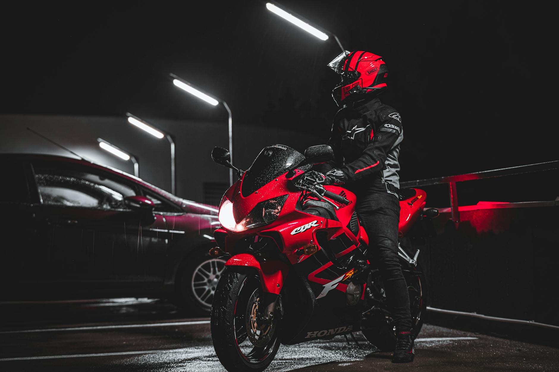 Motocyklista w czerwonym stroju przy czerwonym sporcie w nocnym parkingu