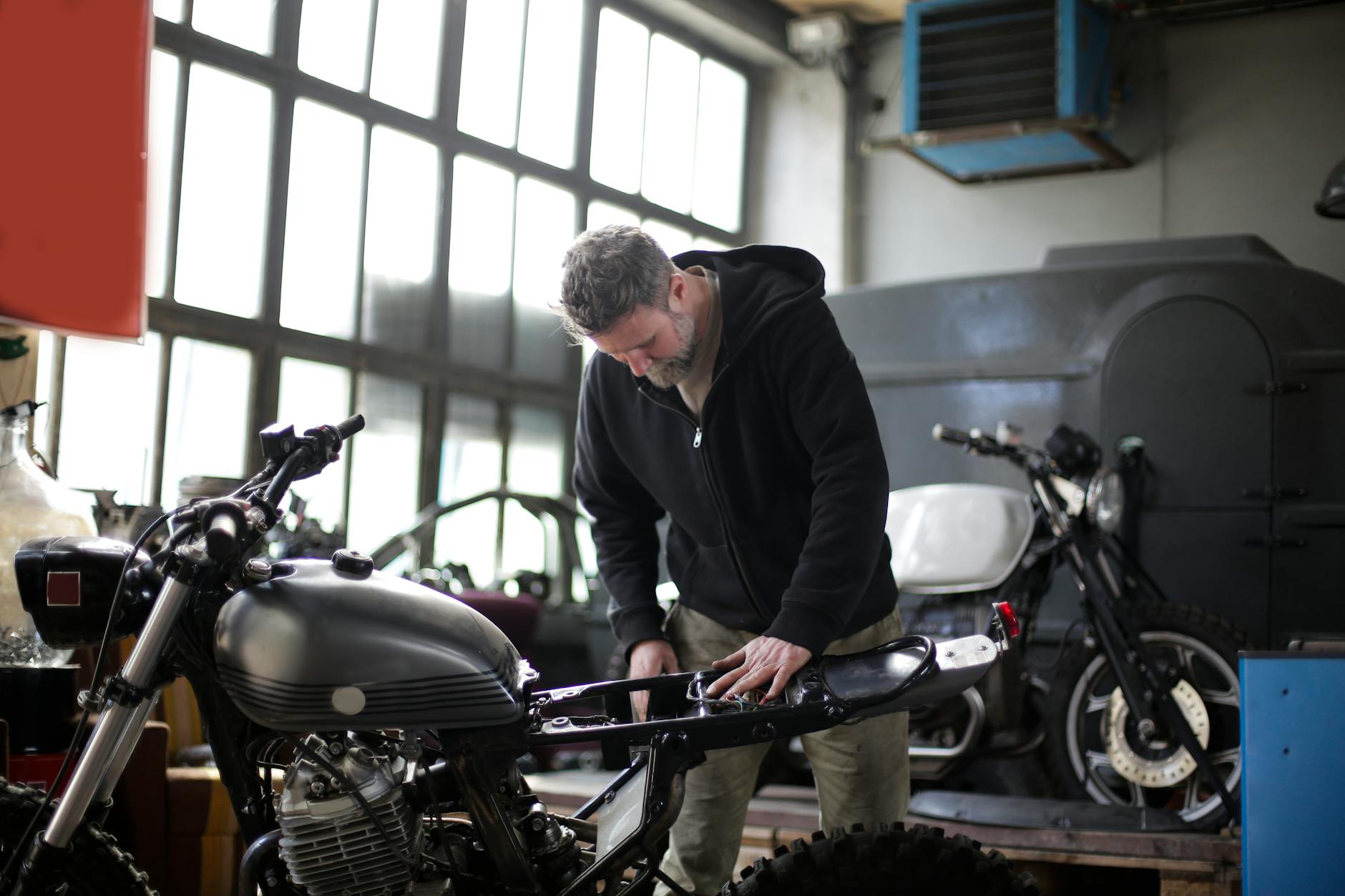 Mechanik w czarnym kombinezonie naprawia motocykl w garażu