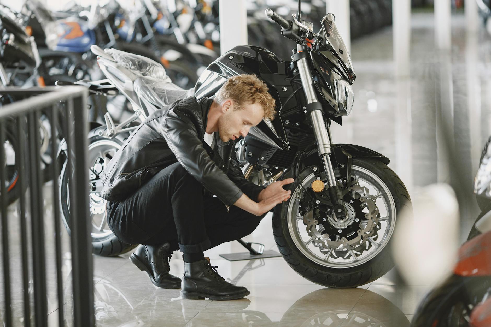 Mężczyzna w skórzanej kurtce ogląda oponę motocykla w salonie