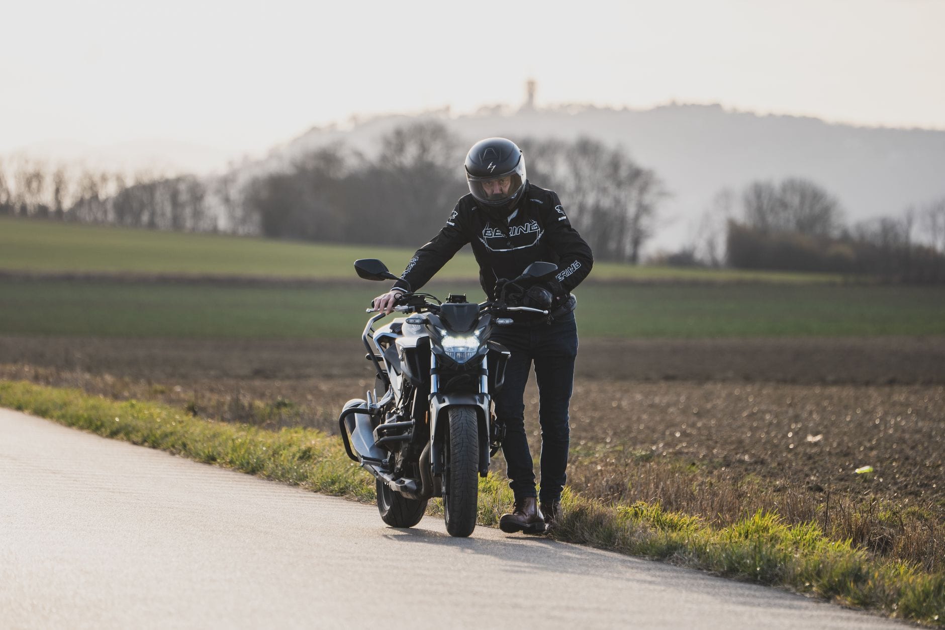 Początkujący motocyklista w kasku stoi obok motocykla przy wiejskiej drodze Początkujący motocyklista w kasku stoi obok motocykla przy wiejskiej drodze
