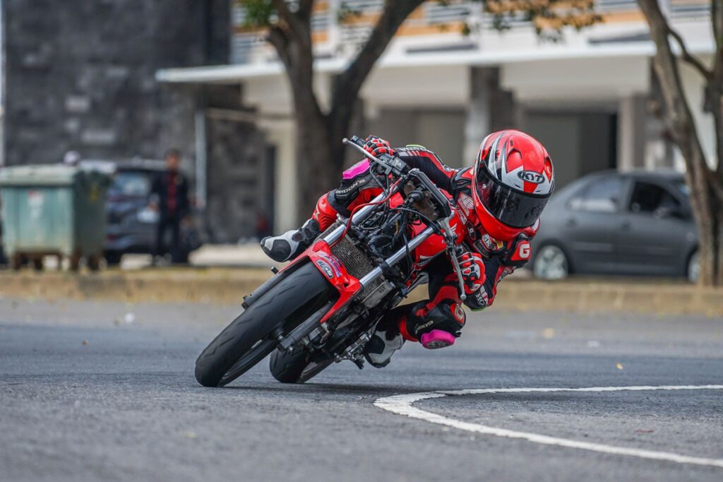 Motocyklista w kolorowym kombinezonie pokonuje ostry zakręt na torze miejskim